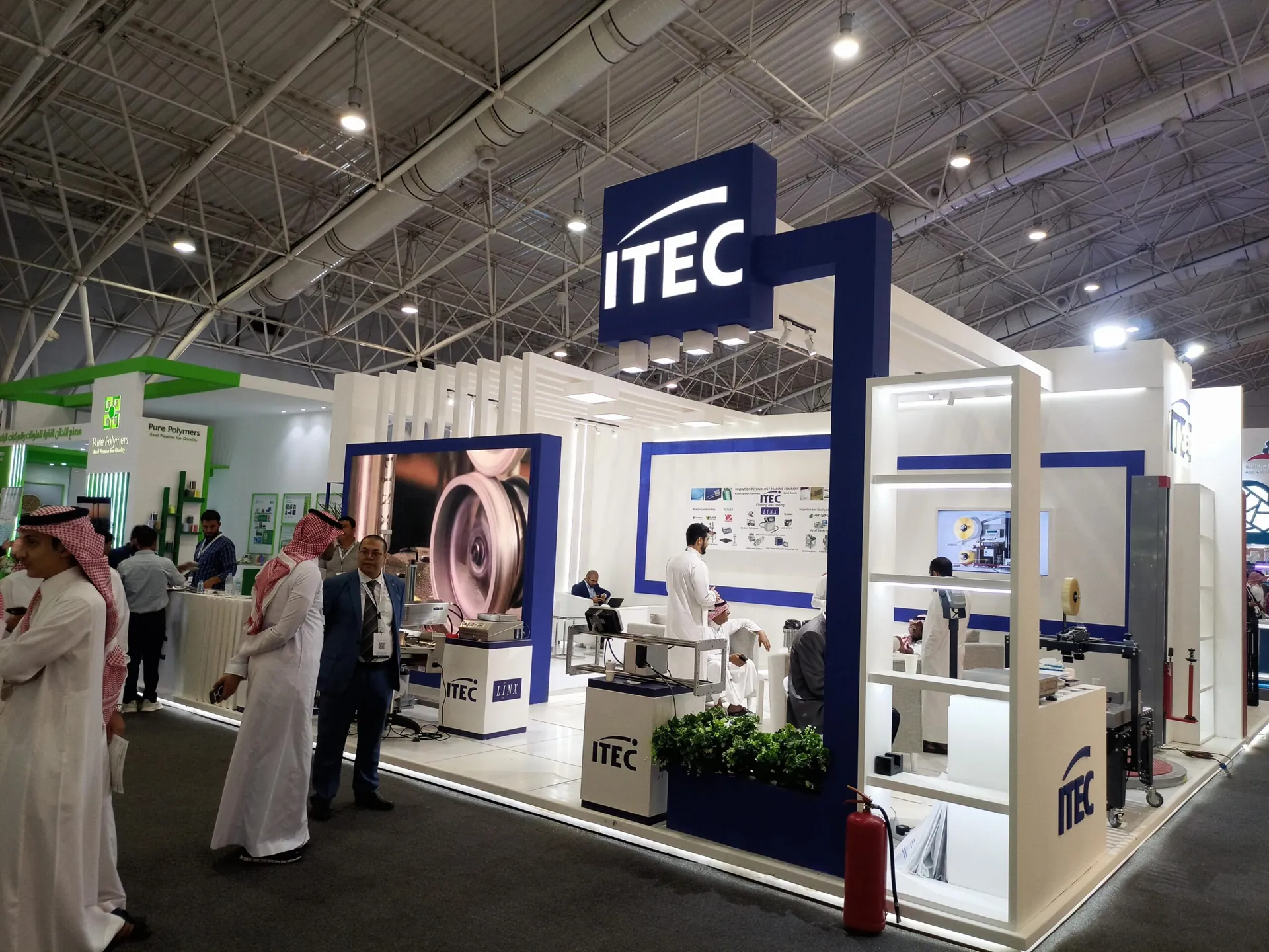 ITEC exhibition stand with a tall lit ITEC sign, white and navy walls and visitors in front