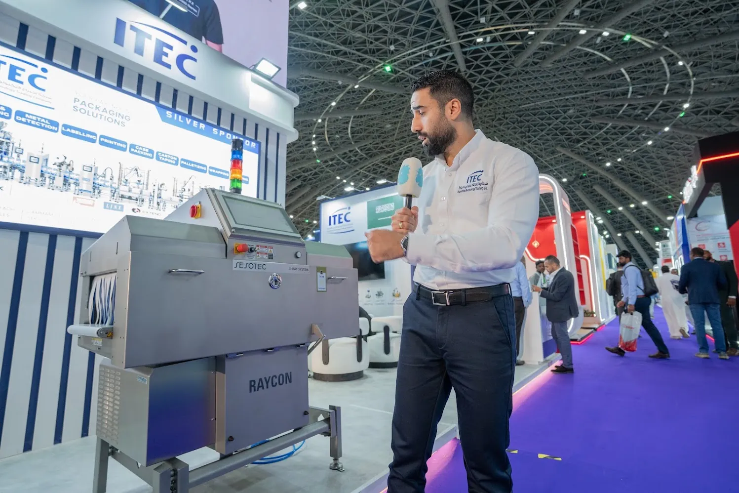 An ITEC presenter speaking beside a machine on the stand, Saudi Food Manufacturing 2026